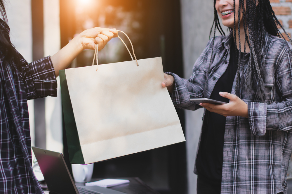 mulher entrega sacola de comprar para outra mulher