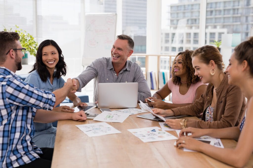 colaboradores em uma mesa de reunião, sorrindo e apertando as mãos