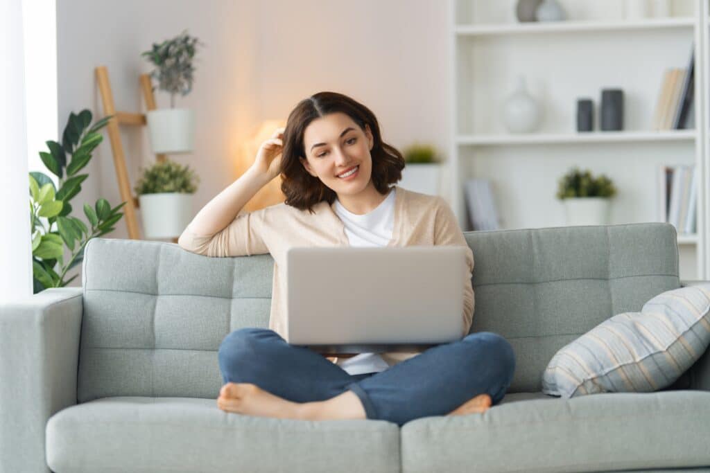 mulher sorrindo, sentada no sofá com o computador no colo