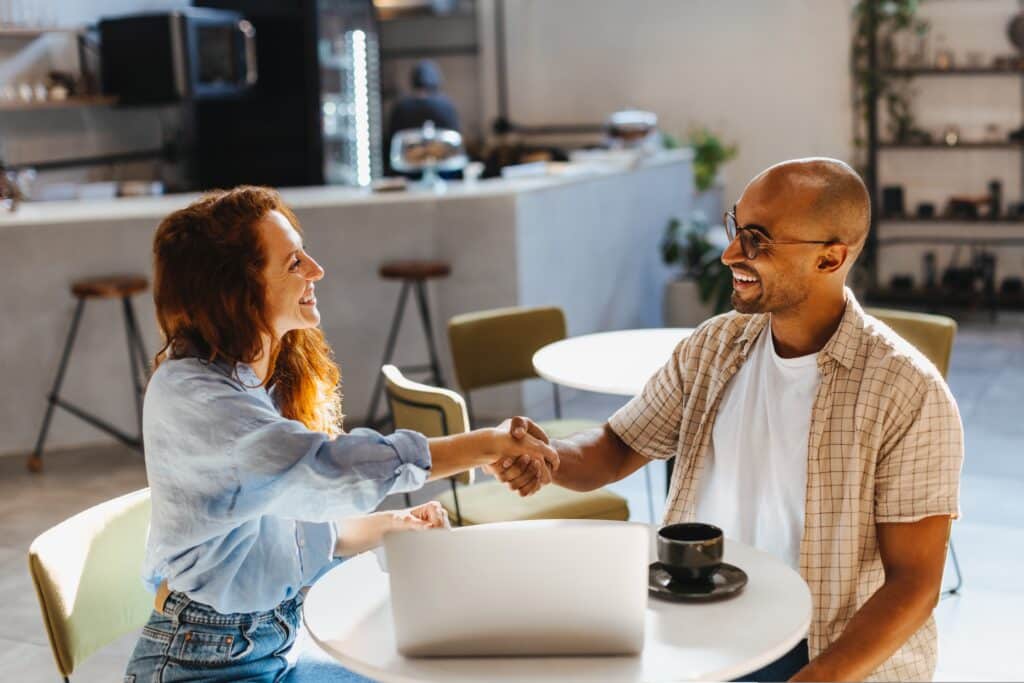 empresários sentados em uma restaurante com um notebook na frente apertando as mãos