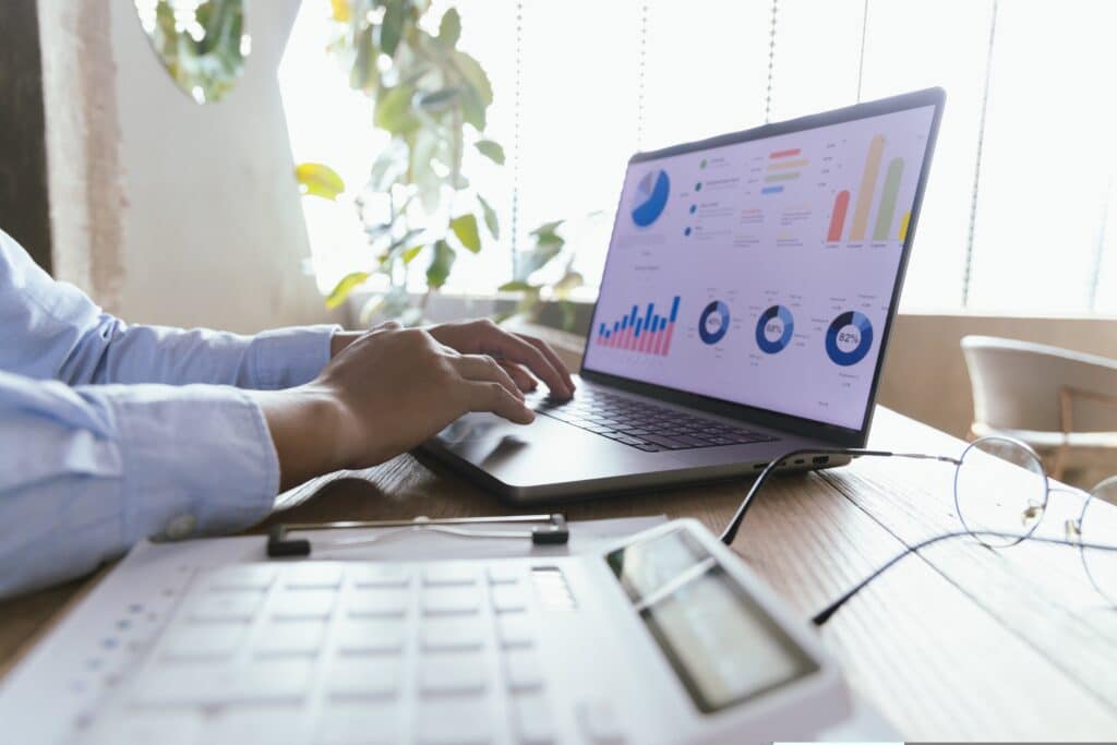 empreendedor trabalhando de frente para o notebook com calculadora na mesa e na tela um dashboard com gráficos financeiros
