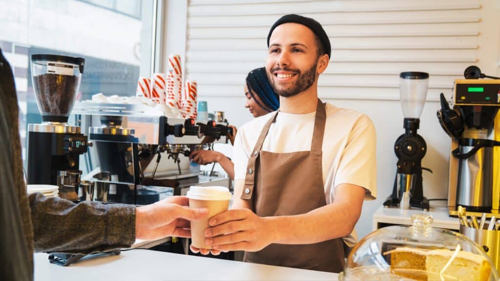 atendente de cafeteria entregando copo de café para um cliente