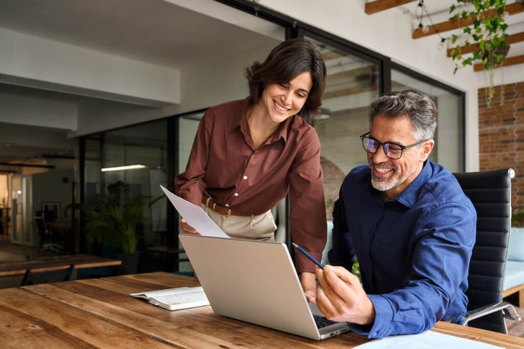 empresários reunidos em frente ao notebook sorrindo e mexendo em papeis