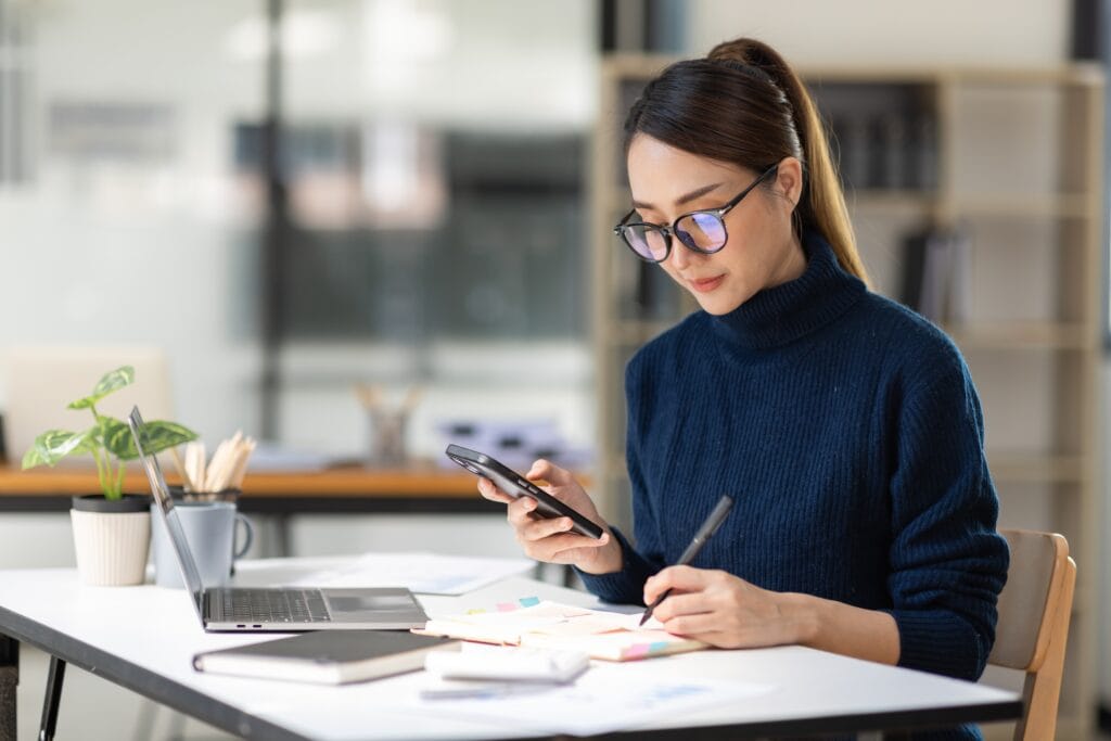 empresária com celular na mão, escrevendo em um caderno